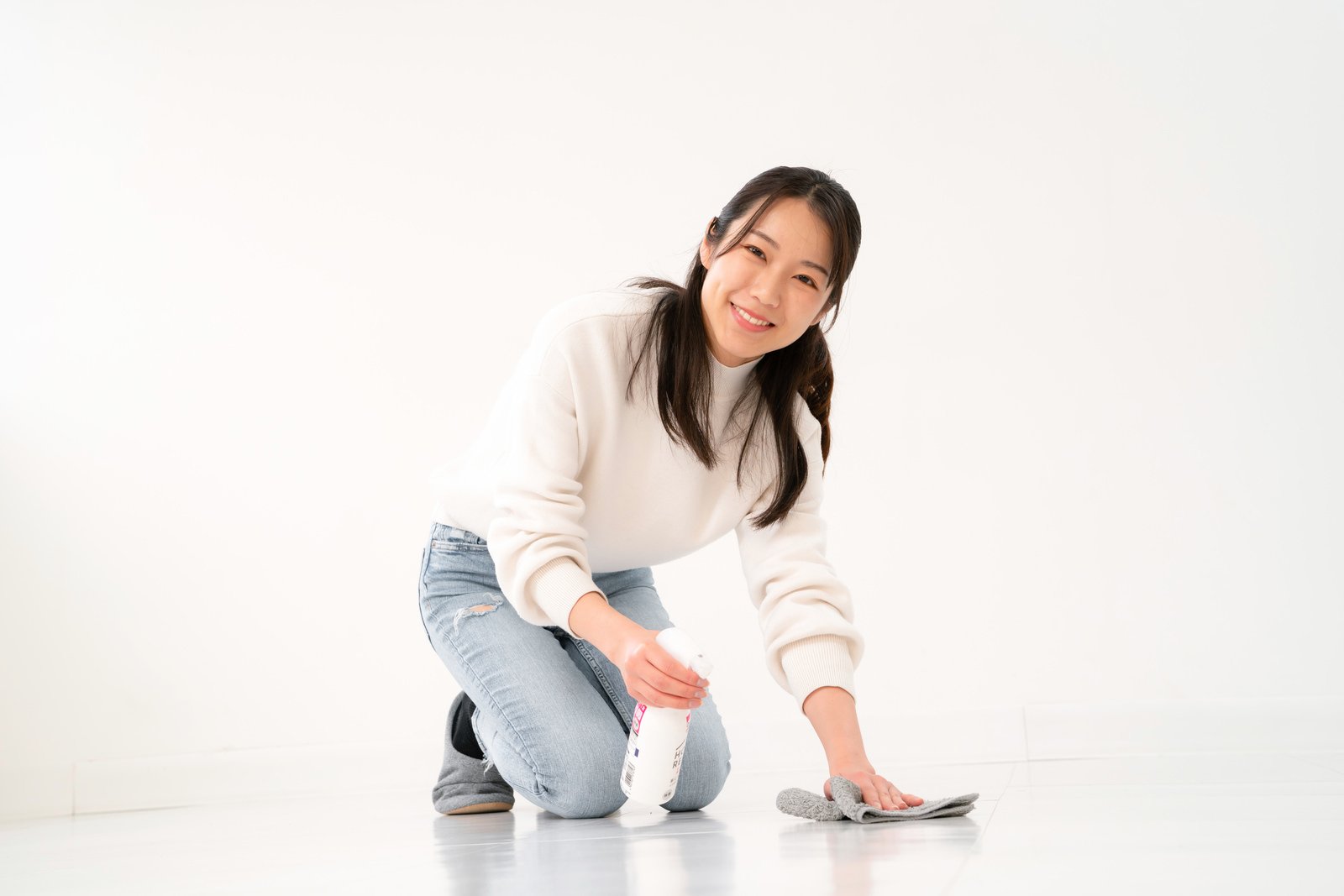 白い部屋で洗剤と布を使い床を掃除する笑顔の女性