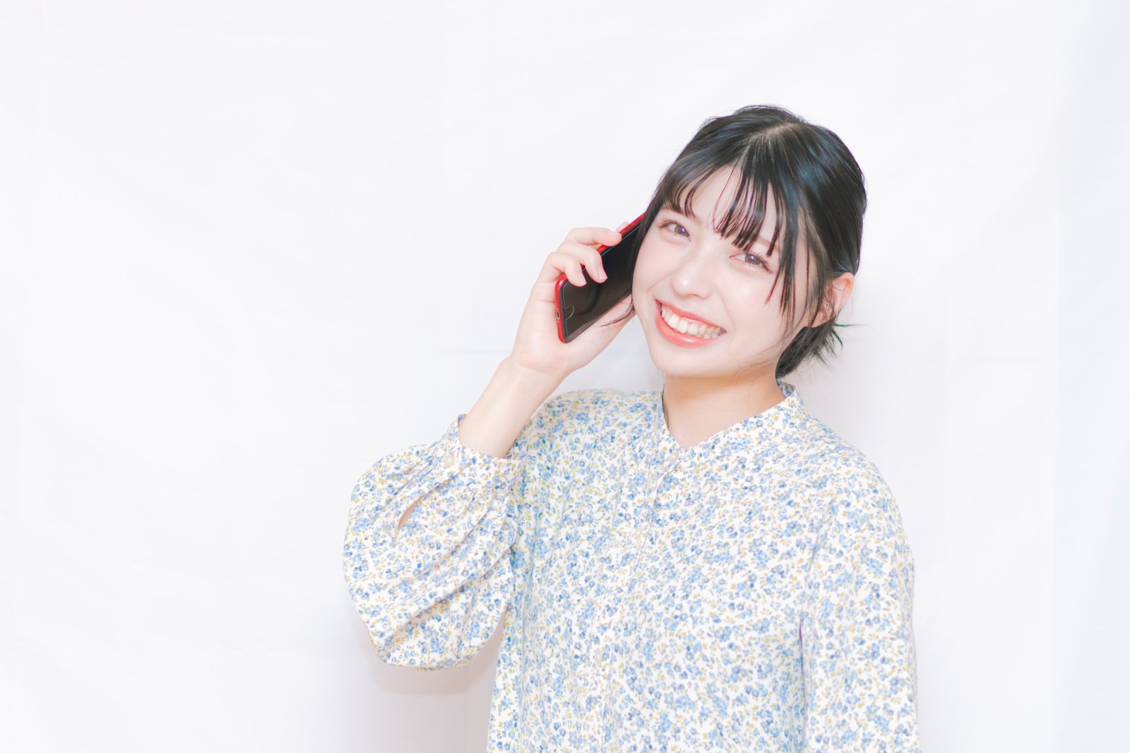 白い背景で花柄の服の女性が笑顔でスマートフォンを耳に当てている