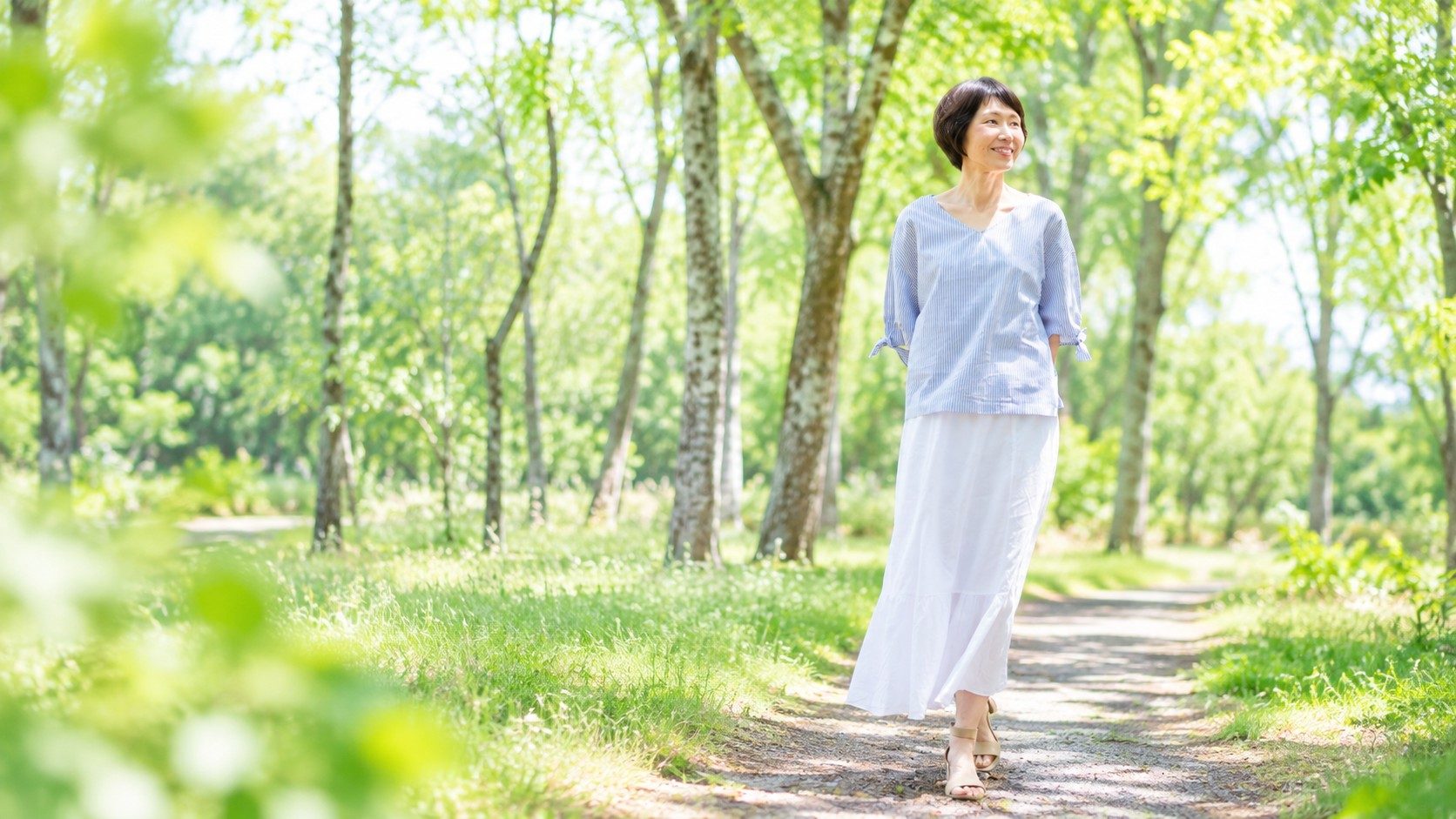 新緑の森の小道を歩く、青い服と白いスカートの女性